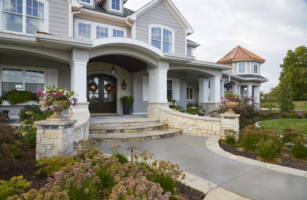 The front entryway and driveway design by Ted Lare Design Build features elegant stone edging and modern cube block accents that add structure and style. Evergreen trees provide year-round greenery, while carefully selected perennial plantings bring vibrant seasonal color, creating a welcoming and polished landscape design in Des Moines