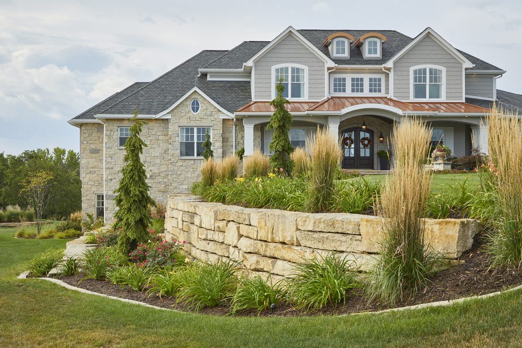 The outdoor landscaping wall by Ted Lare Design Build showcases expertly crafted Unilock stone paired with complementary stone edging. Evergreen tree accents provide structure and year-round interest, while thoughtfully chosen perennial plantings add seasonal color and texture, creating a timeless and inviting landscape design.
