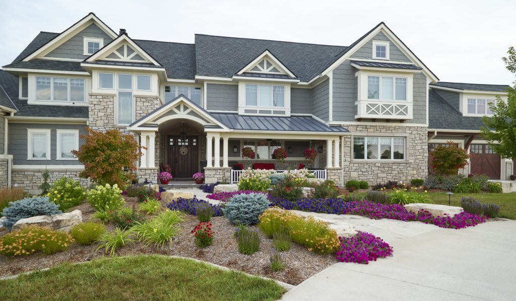 A front entryway featuring a tight-laid flagstone pathway leads to Unilock stone walls, offering a timeless and elegant look with cube accent pieces. Surrounding perennial plantings add vibrant color and texture, creating a welcoming and polished design by Ted Lare Design Build